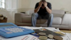 man holds head in hands, credit cards bills money for debt